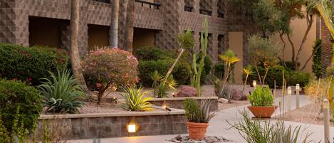 Un patio con un edificio de piedra, diversas plantas y un camino.