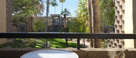 A balcony with a round table and two chairs, overlooking a courtyard with palm trees and a building in the background.