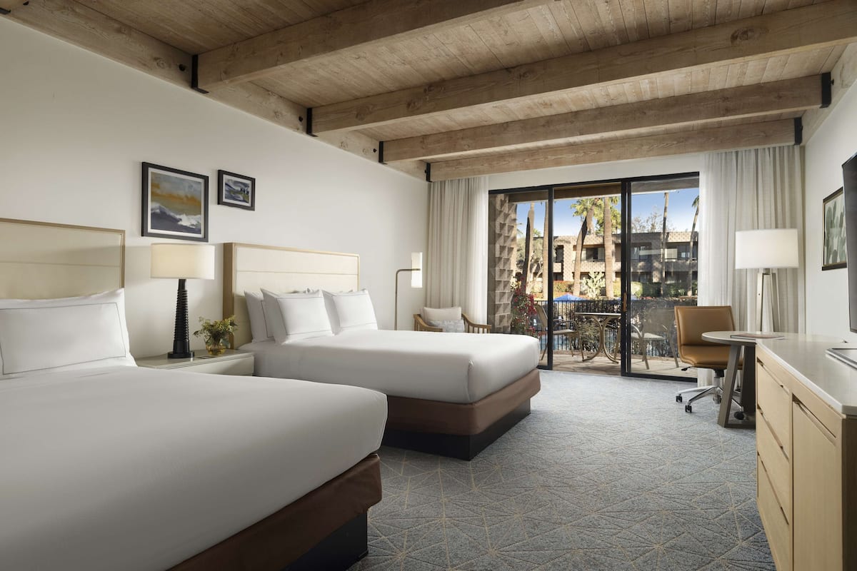 Une chambre d’hôtel avec deux lits, un bureau et un balcon offrant une vue sur les palmiers et les immeubles.