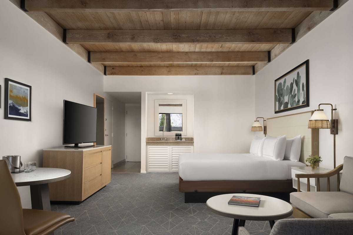 Une chambre d’hôtel moderne avec un plafond en bois, un lit, une télévision, un bureau et un petit coin repas.