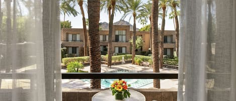 A balcony with a table and chairs, overlooking a pool and palm trees.