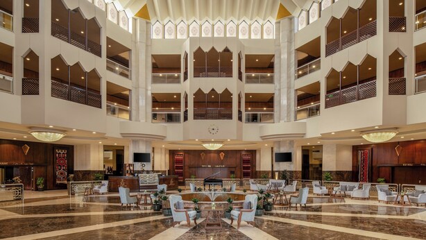 A spacious lobby with a grand piano, multiple seating areas, and a large chandelier.