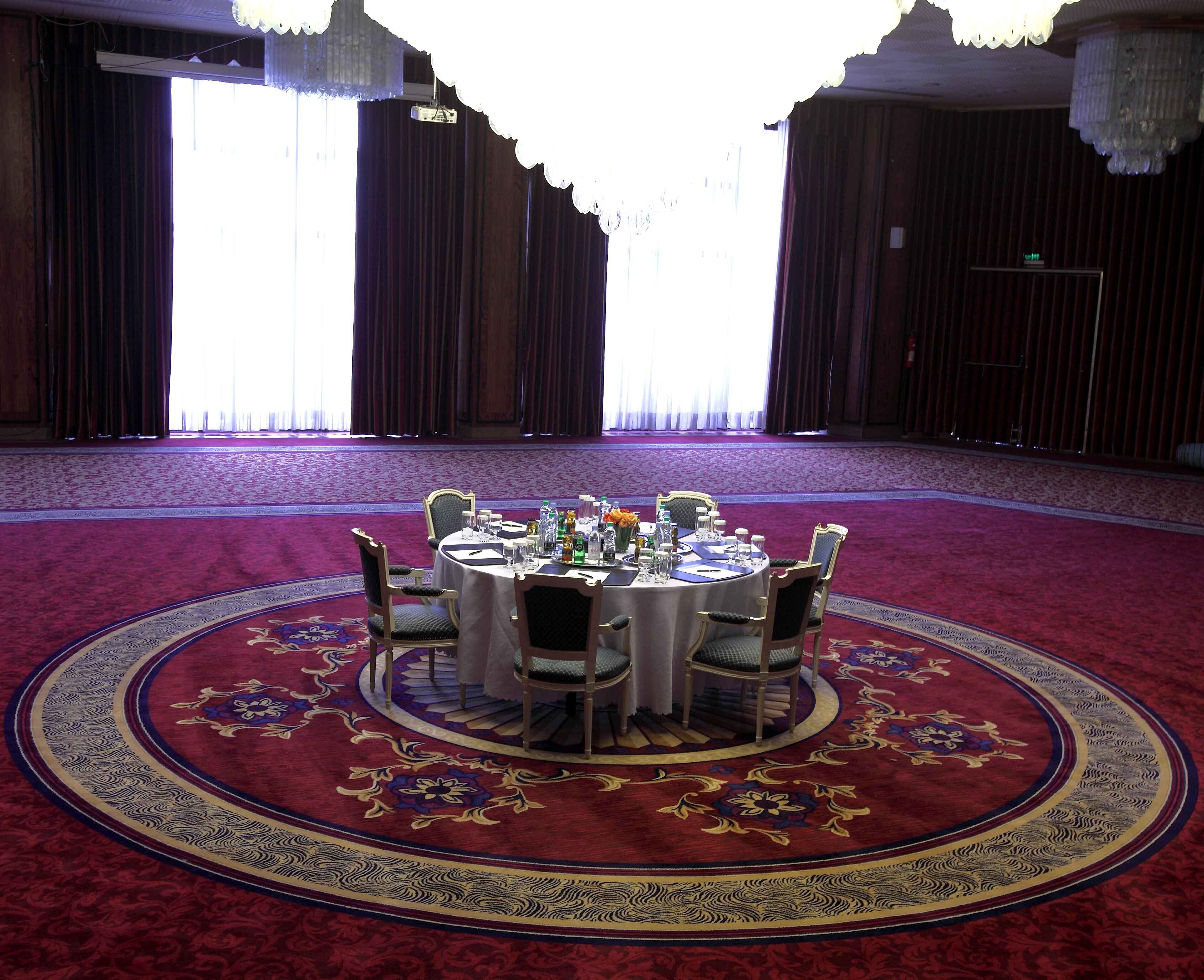 Een ronde tafel voor zes personen, met stoelen, een vloerkleed en een kroonluchter.
