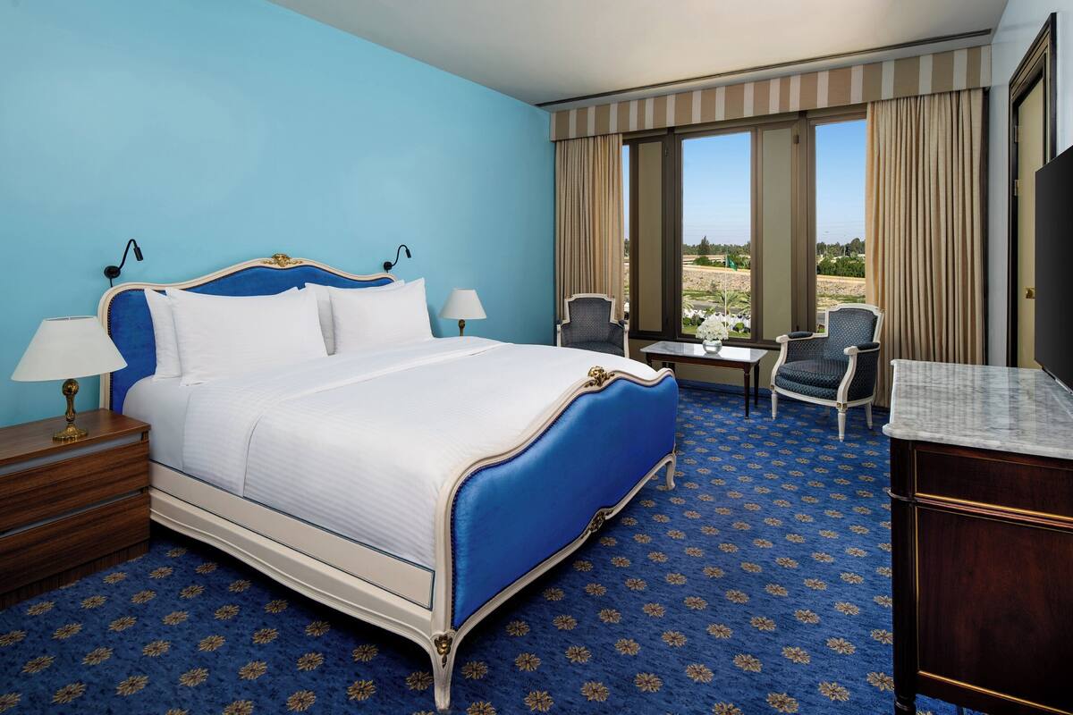 A hotel room with a large bed, a desk, a chair, and a view of the outdoors.