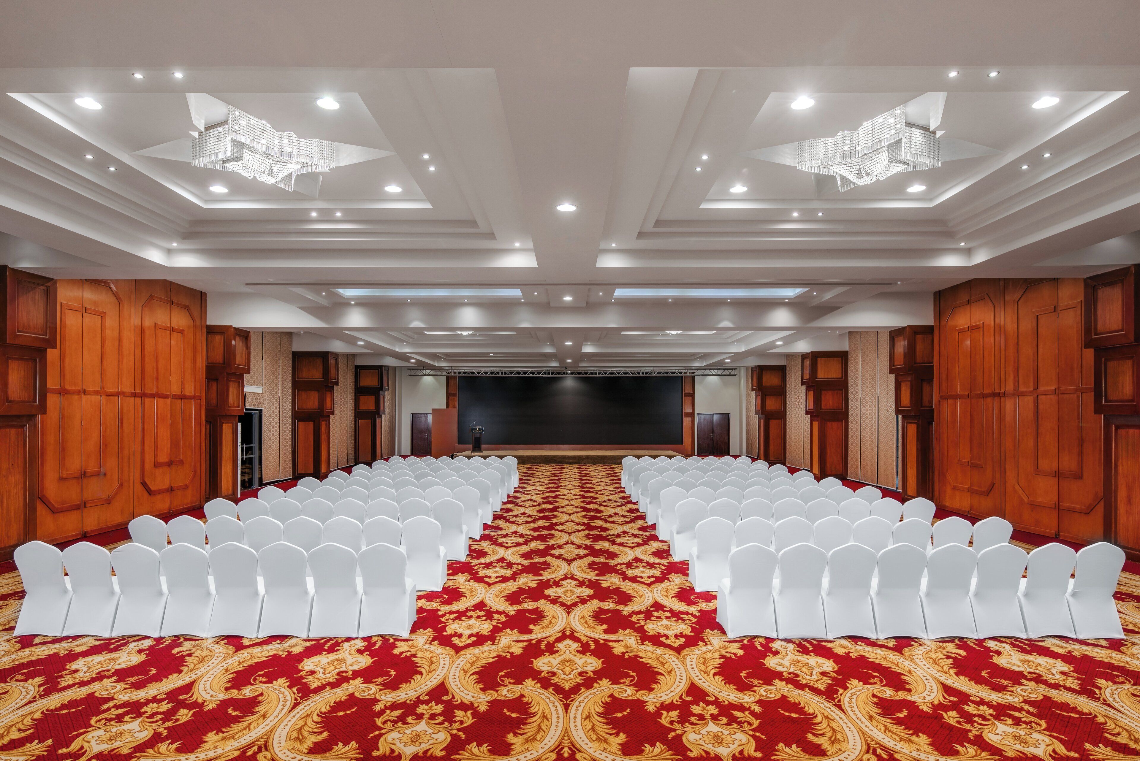 Un salón de conferencias con hileras de sillas blancas, alfombra roja y paneles de madera.