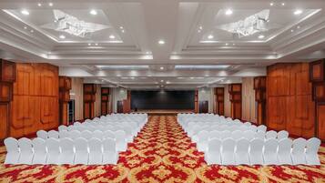 Un salón de conferencias con hileras de sillas blancas, alfombra roja y paneles de madera.