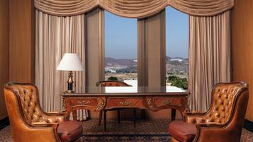 A room with a large desk, two leather chairs, a lamp, and a view of a cityscape through large windows.