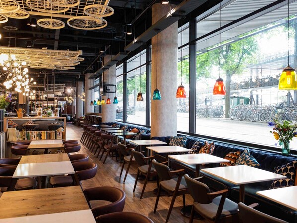 Ein Restaurant mit hoher Decke, großen Fenstern und verschiedenen Sitzmöglichkeiten, darunter Tische und Essecken.