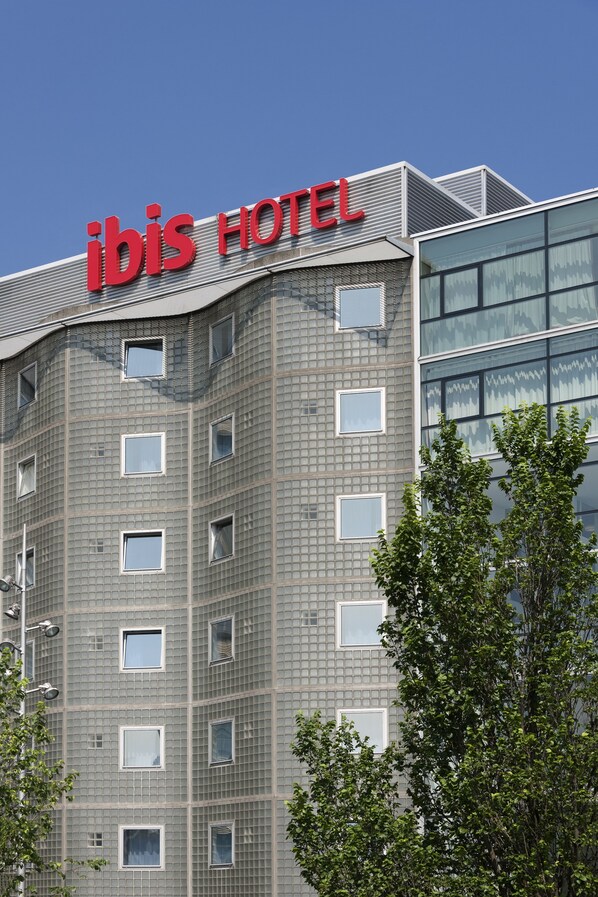 Modernilla designilla varustettu hotellirakennus, jonka katolla on suuri, näkyvästi sijoitettu »ibis HOTEL» -kyltti.