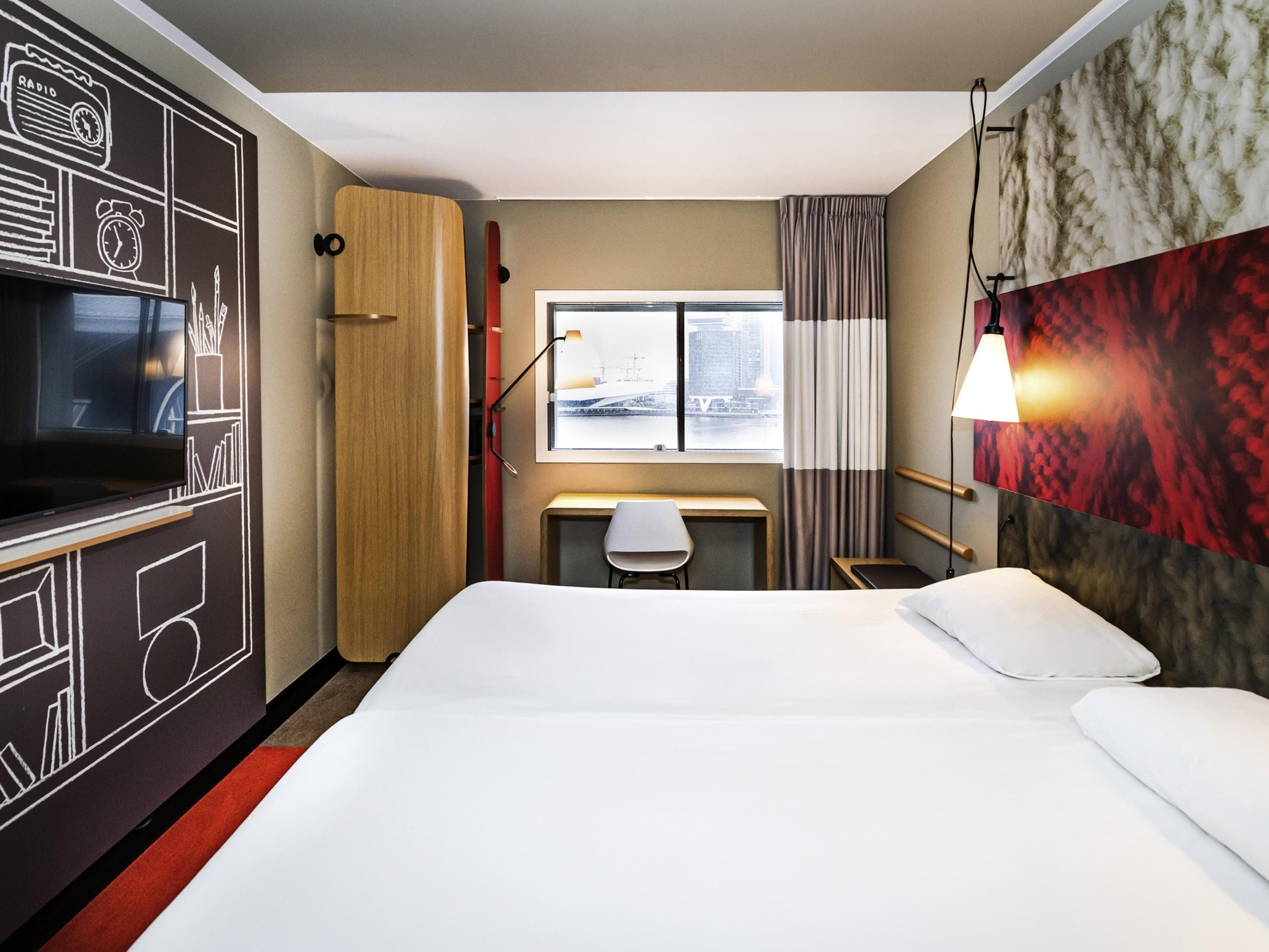 A hotel room with a bed, desk, chair, TV, wardrobe, and a window with a view.