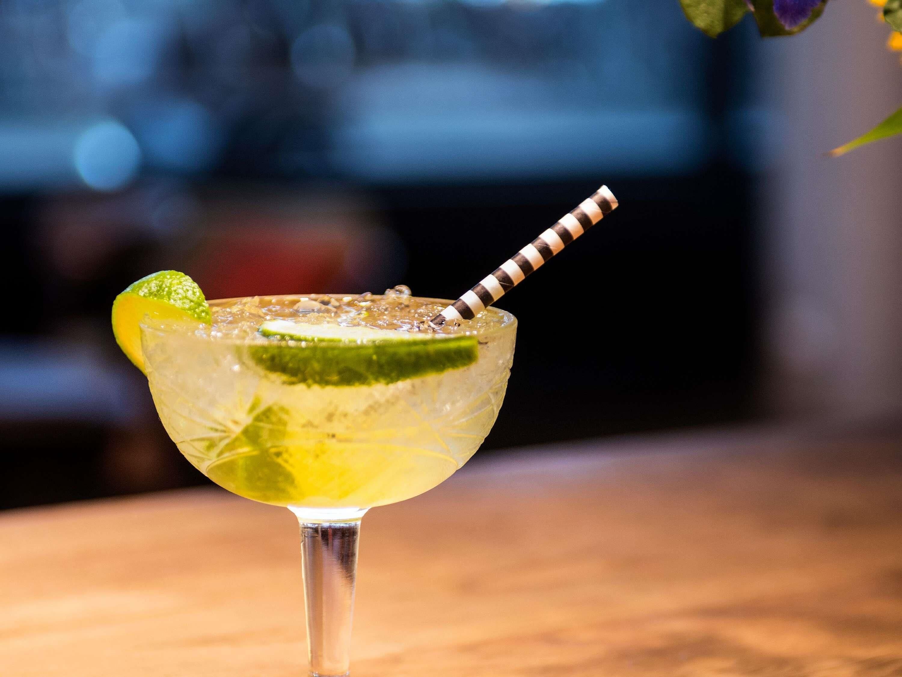 Un cocktail servi dans un verre, agrémenté d’une paille rayée, d’une tranche de citron vert et de glaçons.