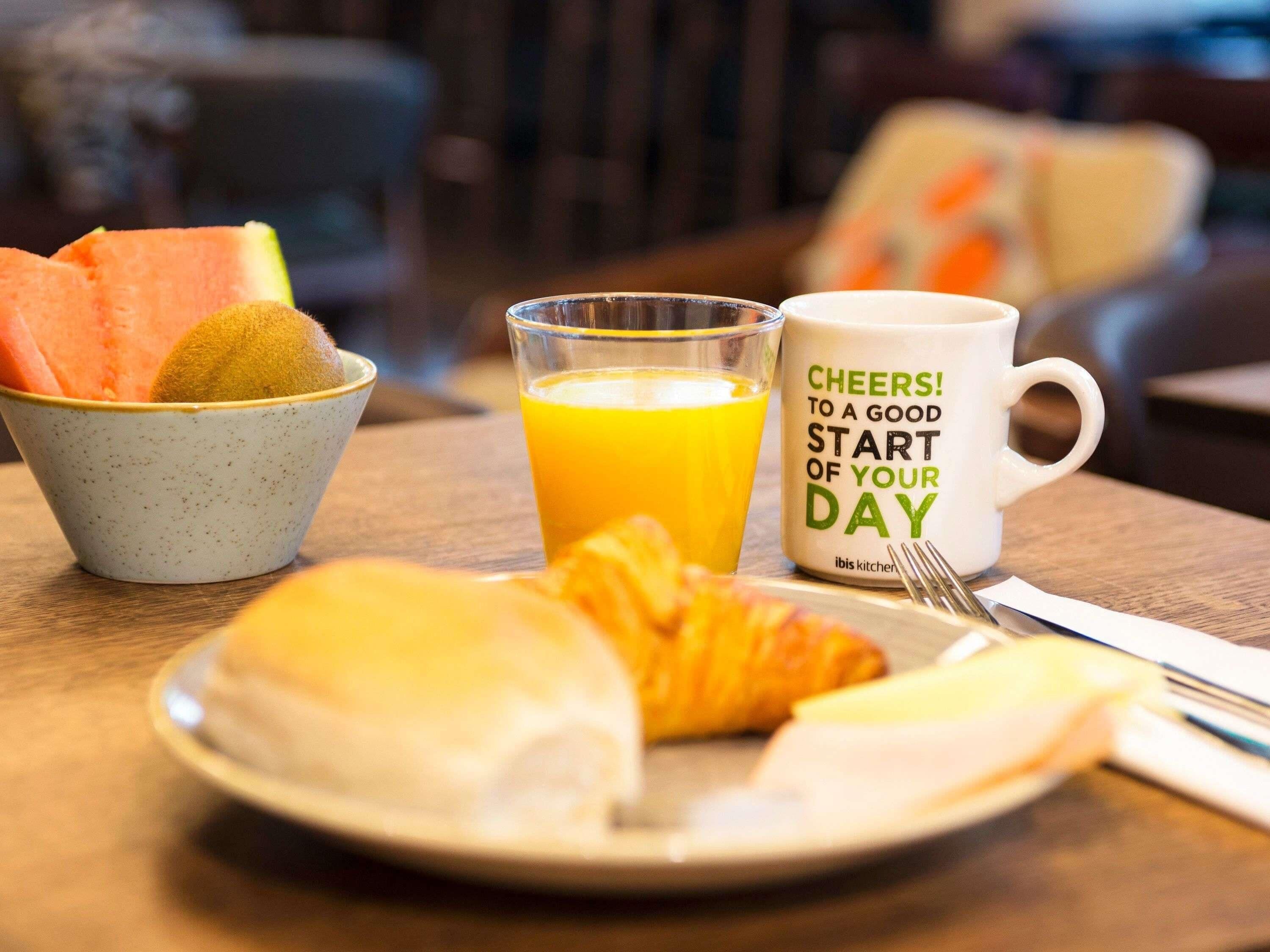 Un desayuno con un croissant, un bol de fruta, un vaso de zumo de naranja y una taza con un mensaje.