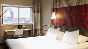 Habitación de hotel con cama, escritorio, silla y vistas a la ciudad desde la ventana.