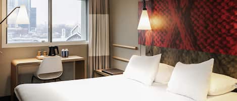 Een hotelkamer met een bed, bureau, stoel en uitzicht op de stad.