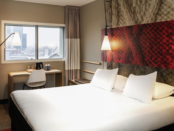 Habitación de hotel con cama, escritorio, silla y vistas a la ciudad desde la ventana.