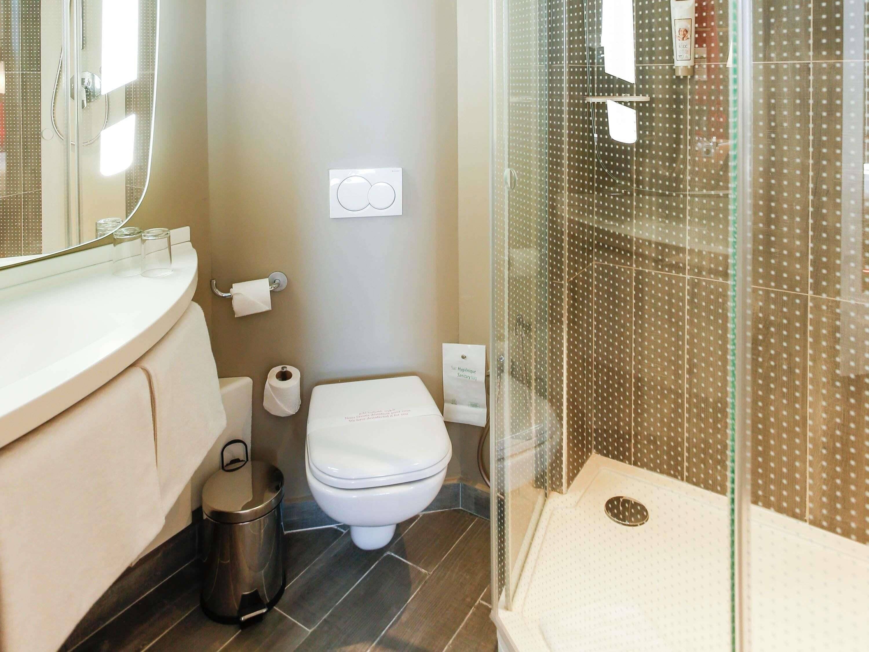 A bathroom with a toilet, a trash bin, a shower enclosure, and a sink.