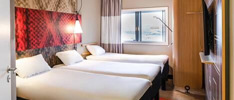 A hotel room with two beds, a large window with curtains, a TV, and a red carpet.