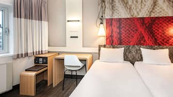 A hotel room with a bed, desk, chair, and a large window with curtains.