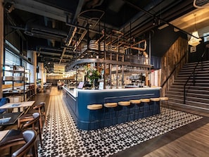 Zona de bar con taburetes, barra y suelo estampado.