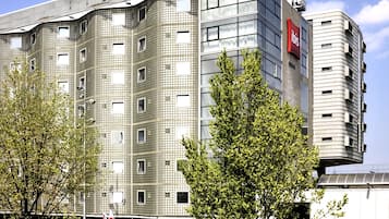Un hôtel moderne, reconnaissable à son grand panneau « IBIS HOTEL », avec de nombreux étages et un parking où sont garés de nombreux vélos.