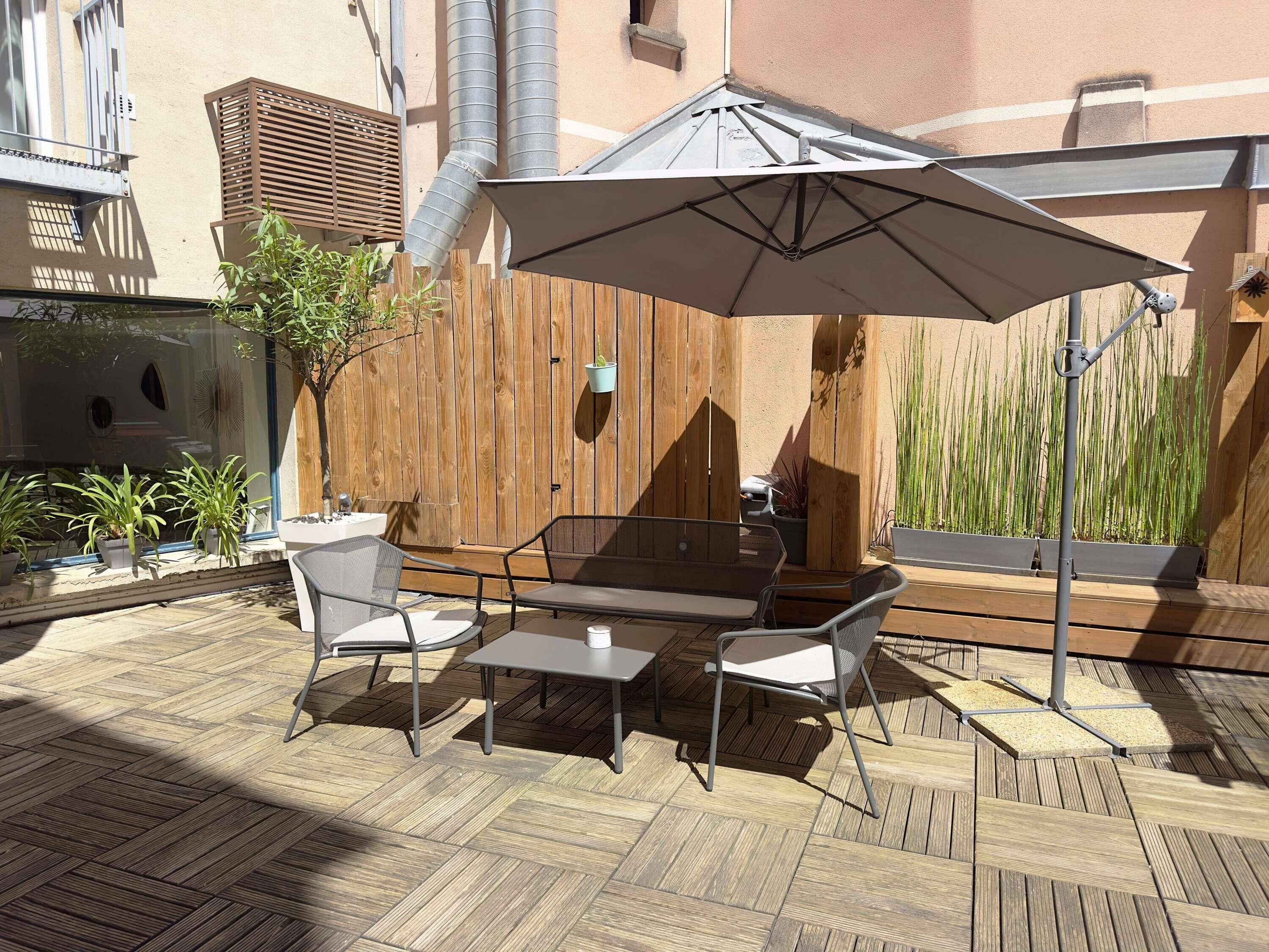 Un patio al aire libre con mesa y sillas, una sombrilla grande y una valla de madera.