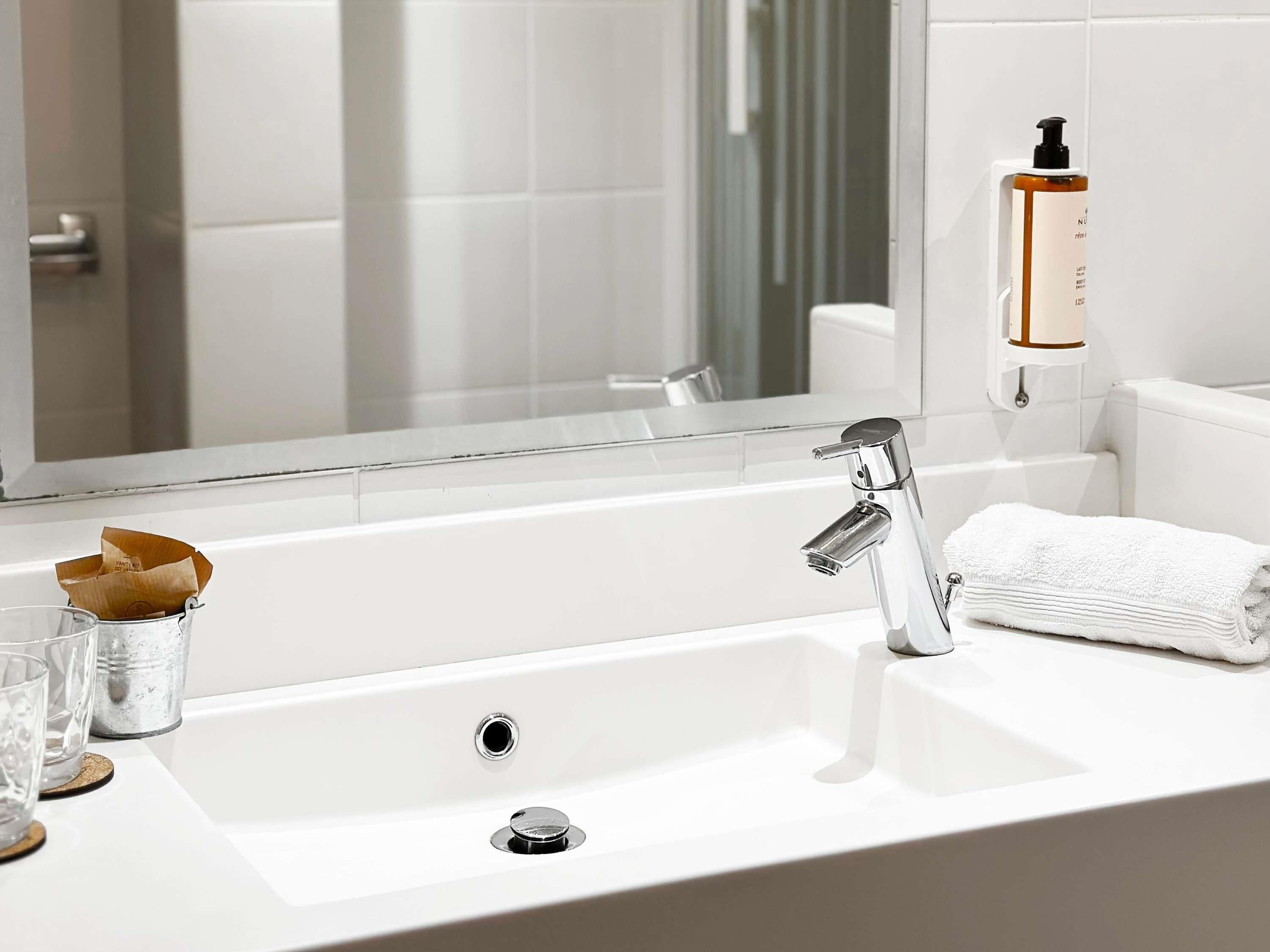 A modern bathroom with a white sink, chrome faucet, and a mirror above it.