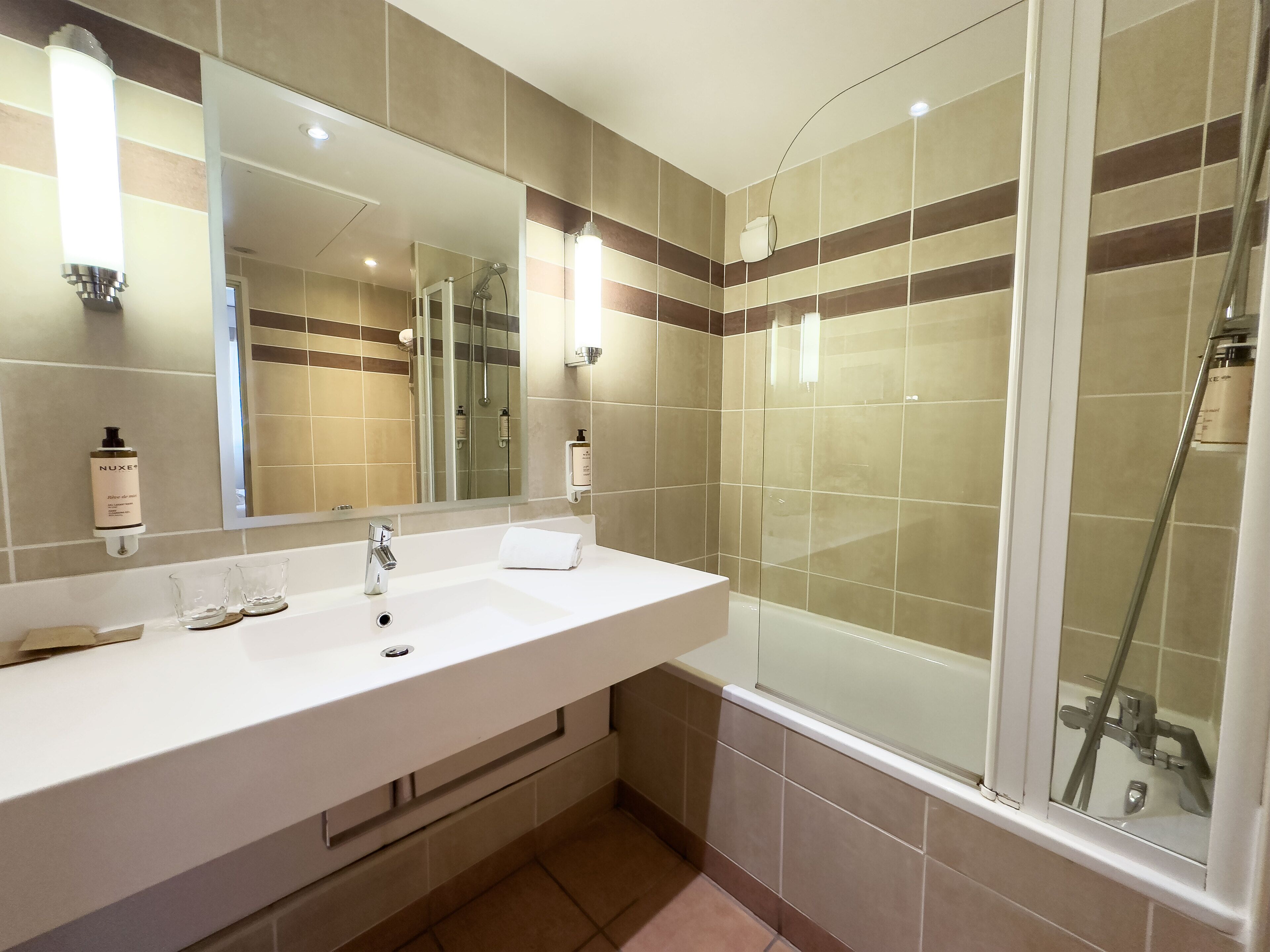 A modern bathroom with a large mirror, a white sink, and a glass-enclosed shower.