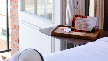 A hotel room with a bed, a window with a view of the outside, and a tray with a welcome card and some food items.