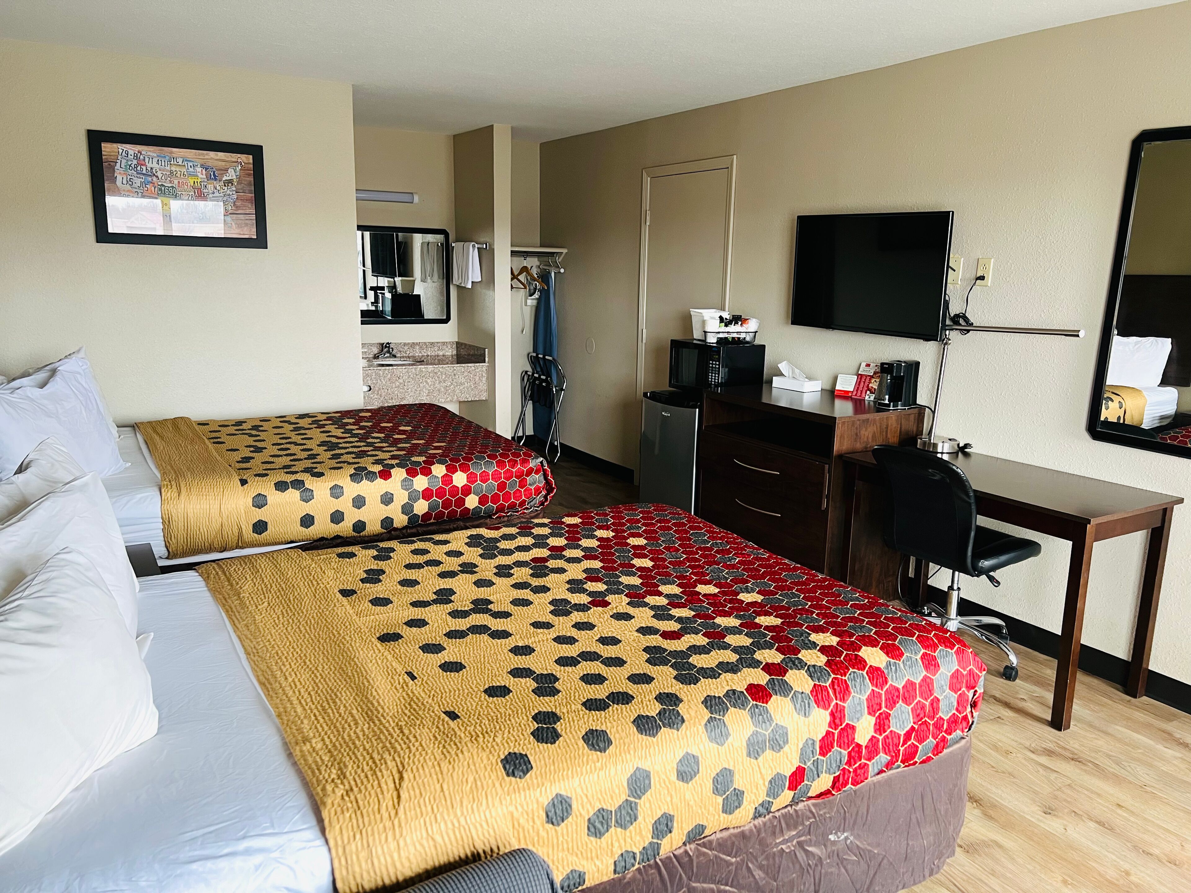 Quarto de hotel com duas camas, uma escrivaninha, uma cadeira, uma televisão e um espelho.