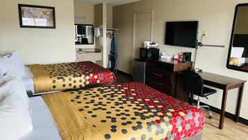 Quarto de hotel com duas camas, uma escrivaninha, uma cadeira, uma televisão e um espelho.