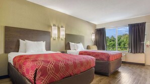 A hotel room with two beds, each with a red patterned bedspread, a wooden floor, and a large window with curtains. - Econo Lodge Fort Knox (Radcliff)