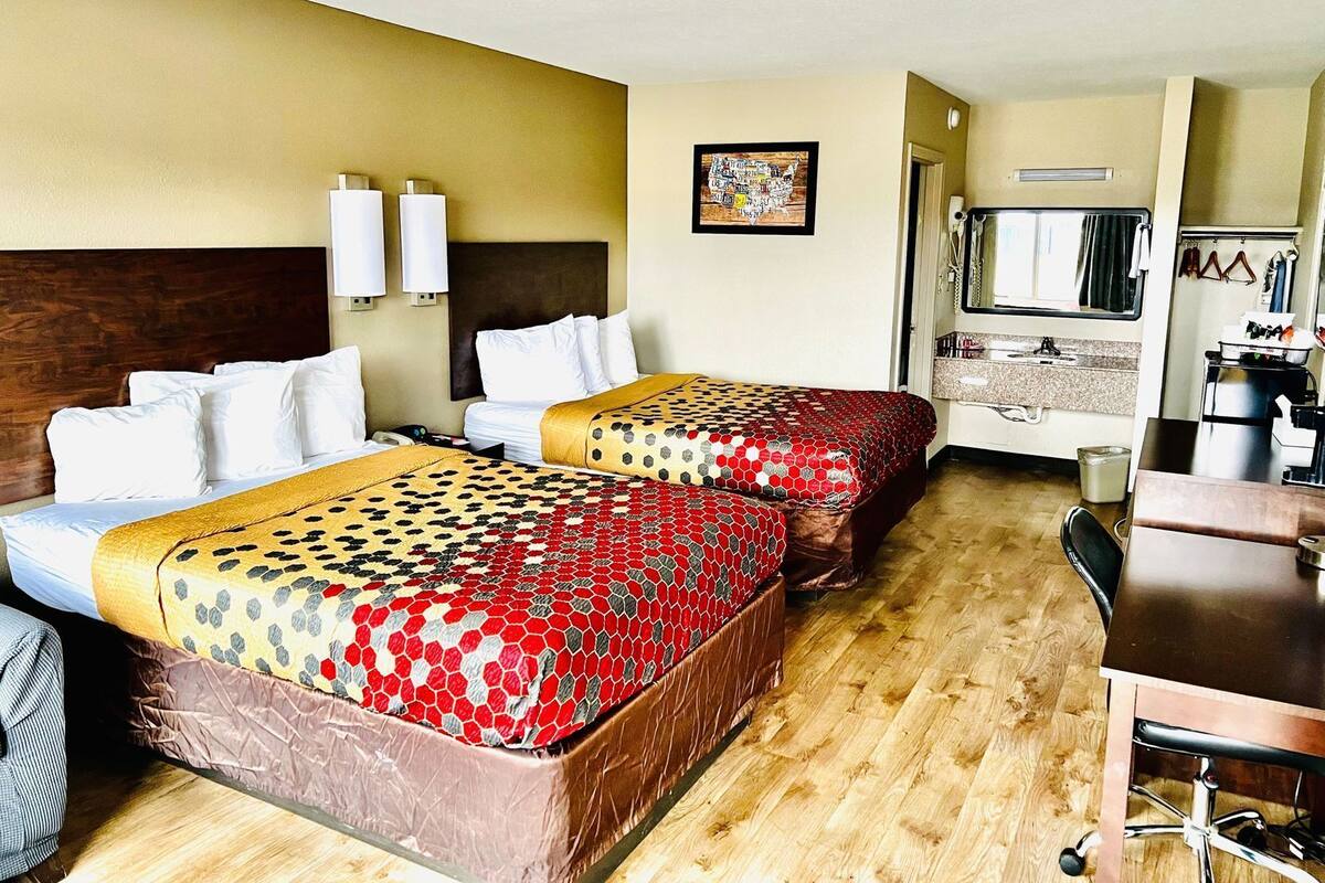 A hotel room with two beds, a desk, a mirror, and a bathroom visible through an open door.