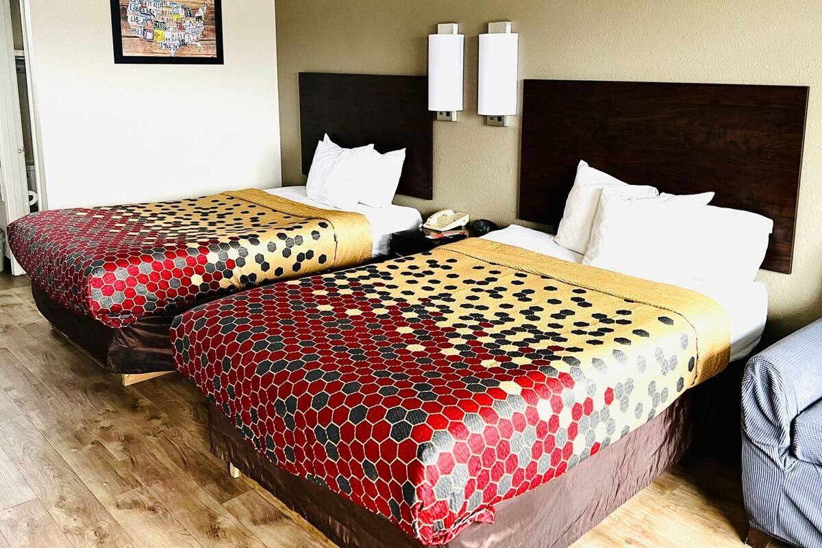 A hotel room with two beds, a nightstand, a telephone, and a wall-mounted light fixture.