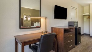 A compact hotel room with a wooden desk, a black leather chair, a flat-screen TV mounted on the wall, a small refrigerator, and a microwave on top of the fridge. - Econo Lodge Fort Knox (Radcliff)