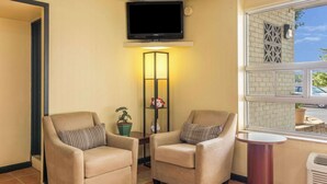 A room with two beige armchairs, a flat-screen TV mounted on the wall, a tall floor lamp, and a window with a view of the outside. - Econo Lodge Fort Knox (Radcliff)