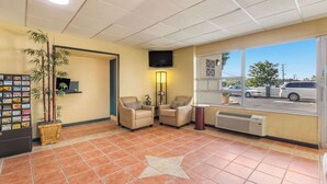 A reception area with a tiled floor, two armchairs, a television mounted on the wall, a window with a view of parked cars, and a wall-mounted shelf with various items. - Econo Lodge Fort Knox (Radcliff)