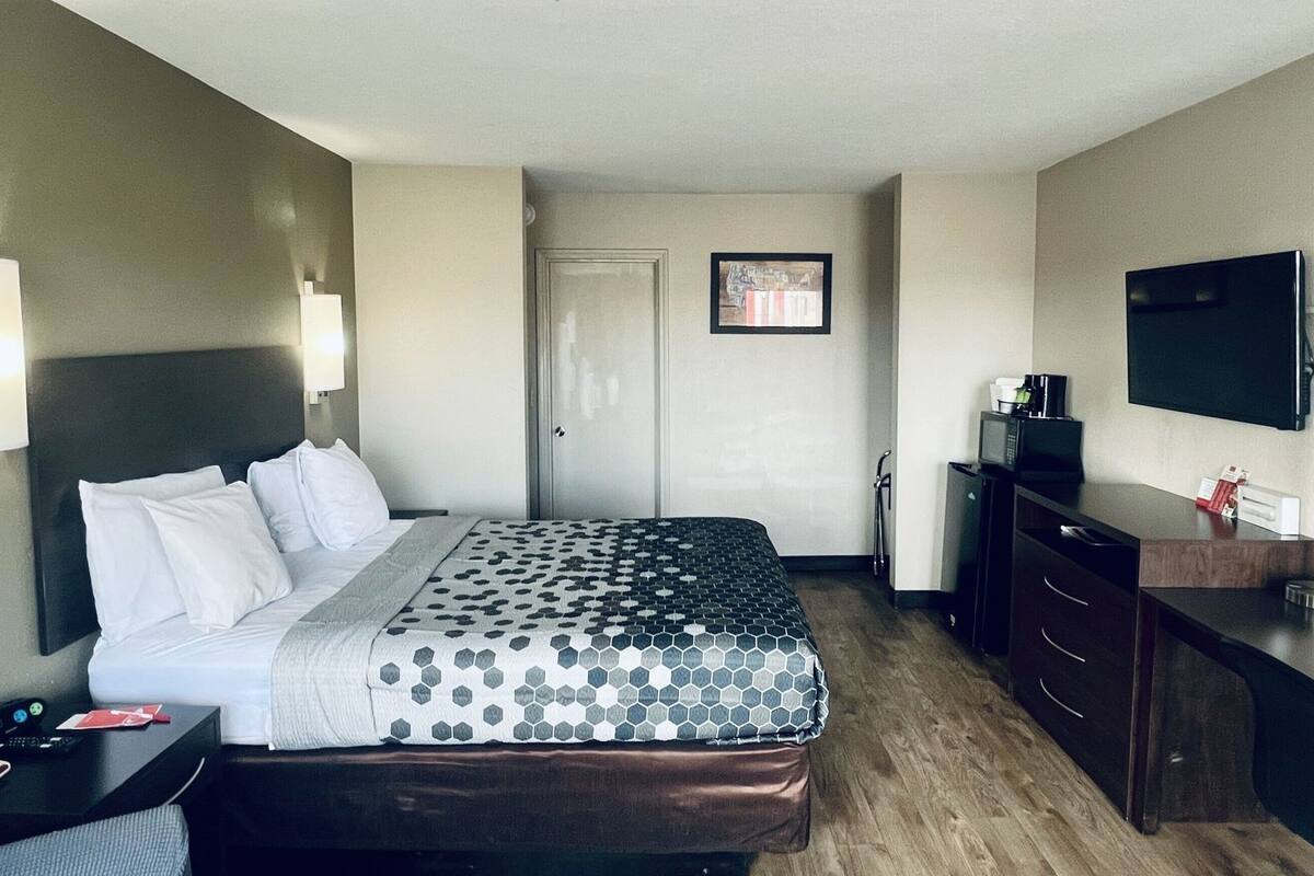 A hotel room with a bed, bedside tables, a desk, a dresser, a TV, and a door.