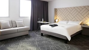 A hotel room with a bed, a sofa, a small table, and a window with curtains.