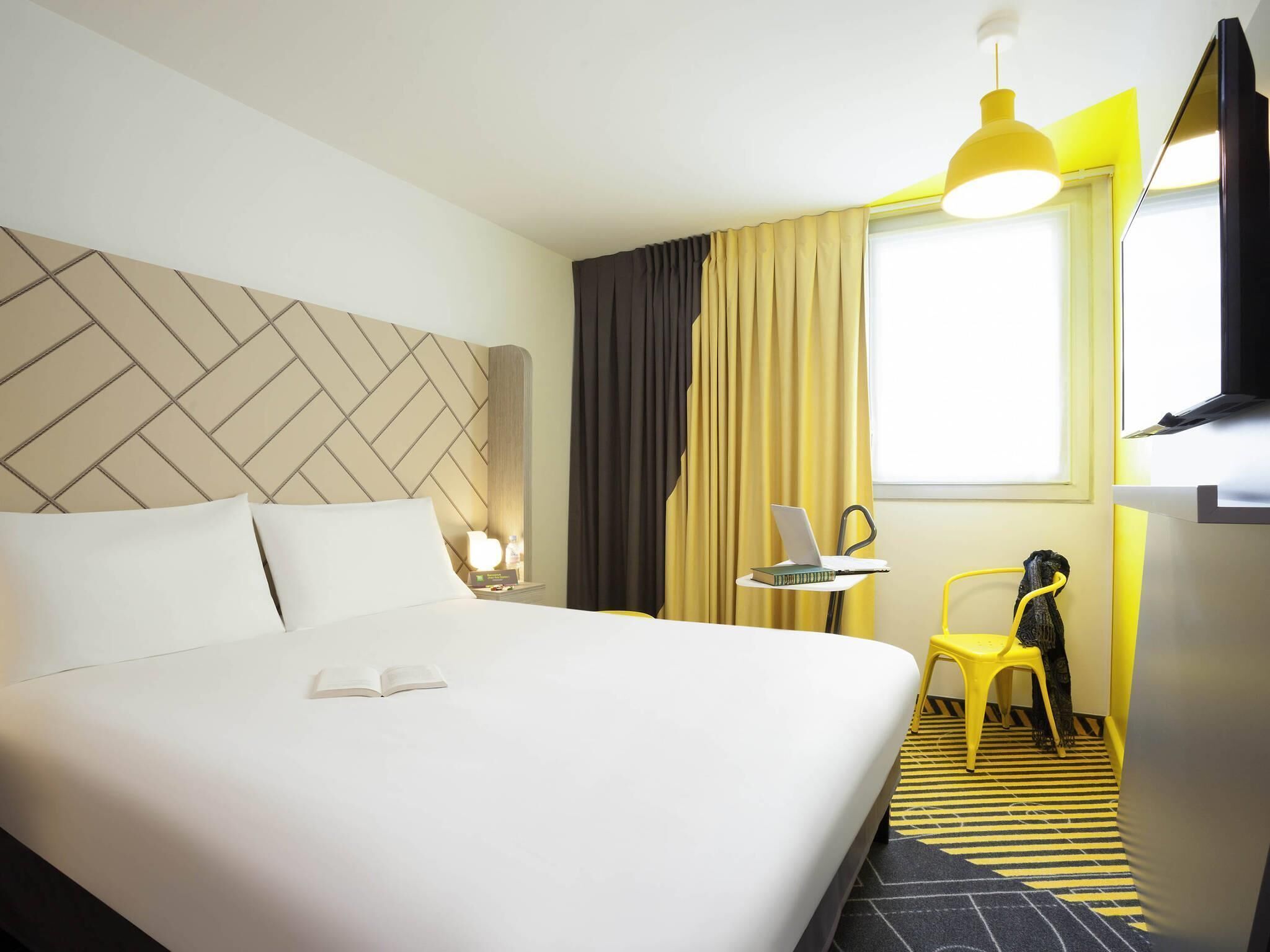 Una habitación de hotel con una cama, un escritorio con una computadora portátil, una silla y un televisor.
