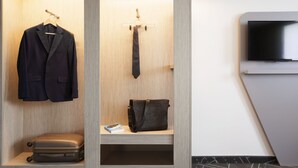 A hotel room with a wardrobe containing a suit, tie, handbag, and suitcase.