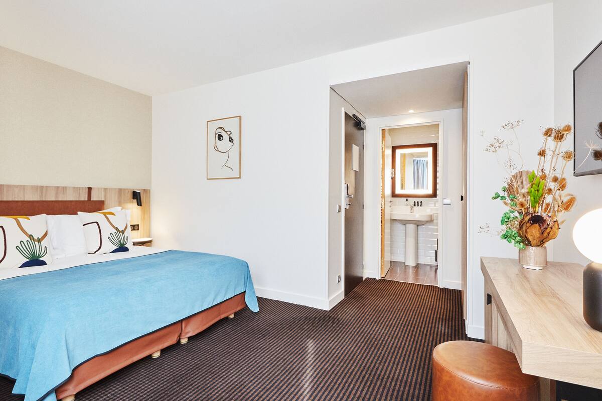 A hotel room with a bed, bedside table, and a bathroom visible through an open door.