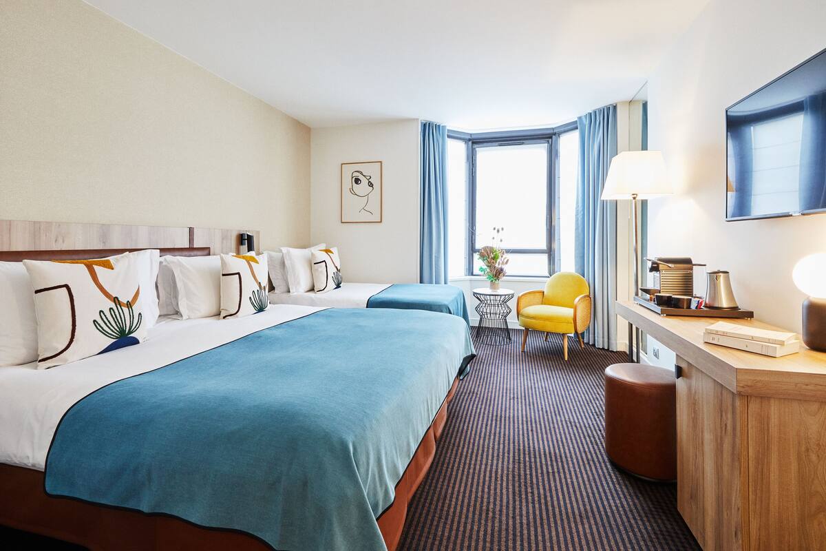 A hotel room with two beds, a desk, a chair, a TV, and a window with curtains.