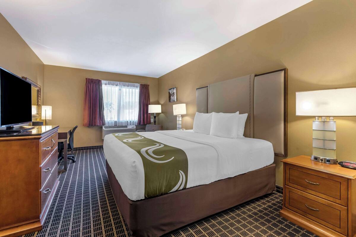 A hotel room with a large bed, a desk with a chair, a TV, and a dresser.