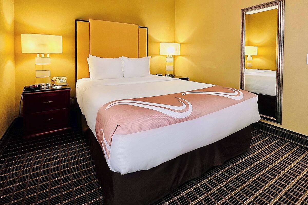 A hotel room with a large bed, two bedside tables with lamps, a mirror, and a patterned carpet.