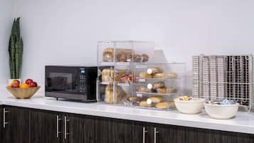 Een aanrecht met een magnetron, doorzichtige bakken vol muffins en een schaal met fruit.