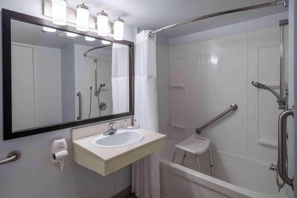 A modern bathroom with a white sink, a large mirror, a handheld showerhead, and a grab bar.