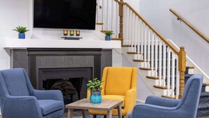 Una sala de estar con chimenea, dos sillones, una mesa de centro y un televisor sobre la chimenea.