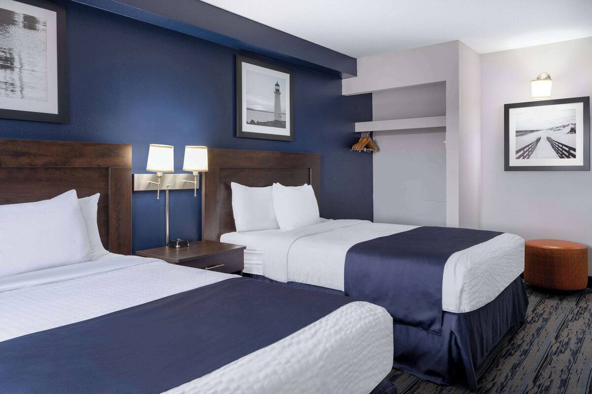 A hotel room with two beds, a nightstand, a lamp, and framed pictures on the walls.