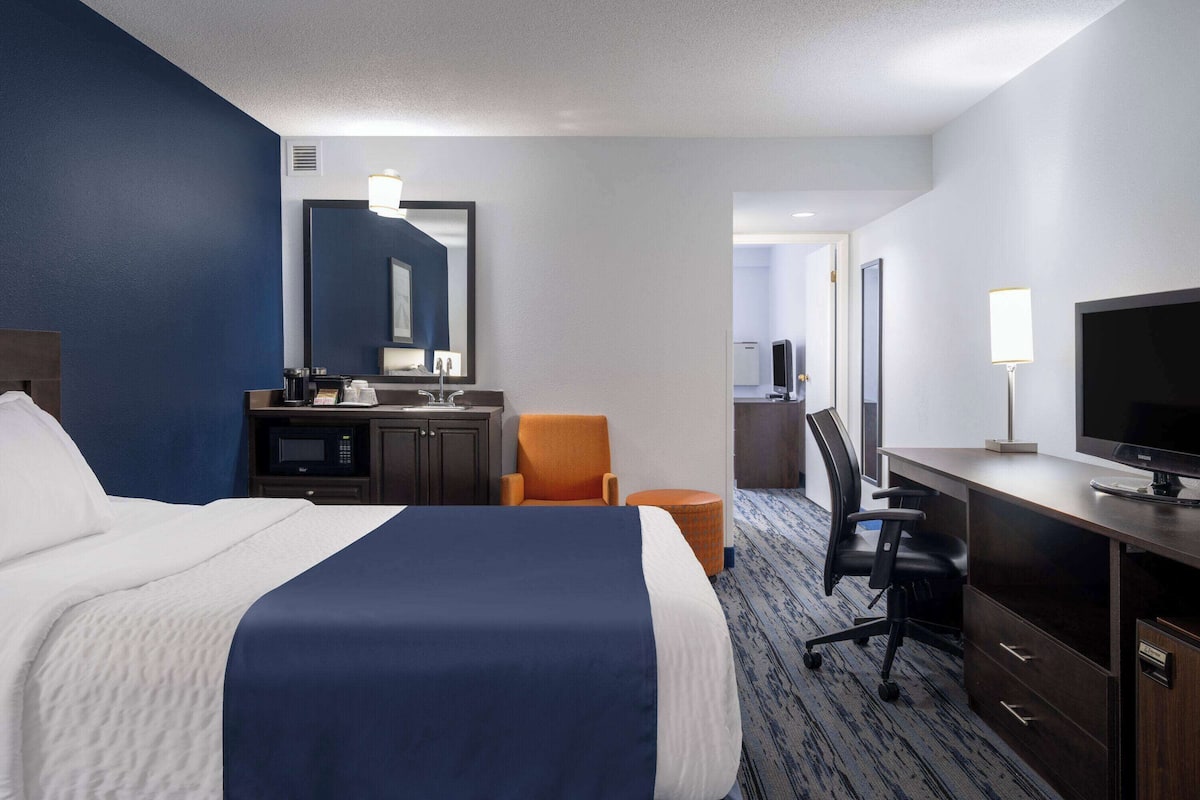 A hotel room with a large bed, a desk with a computer, a chair, a TV, and a microwave.