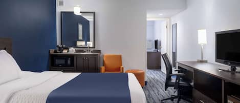 A hotel room with a large bed, a desk with a computer, a chair, a TV, and a microwave.